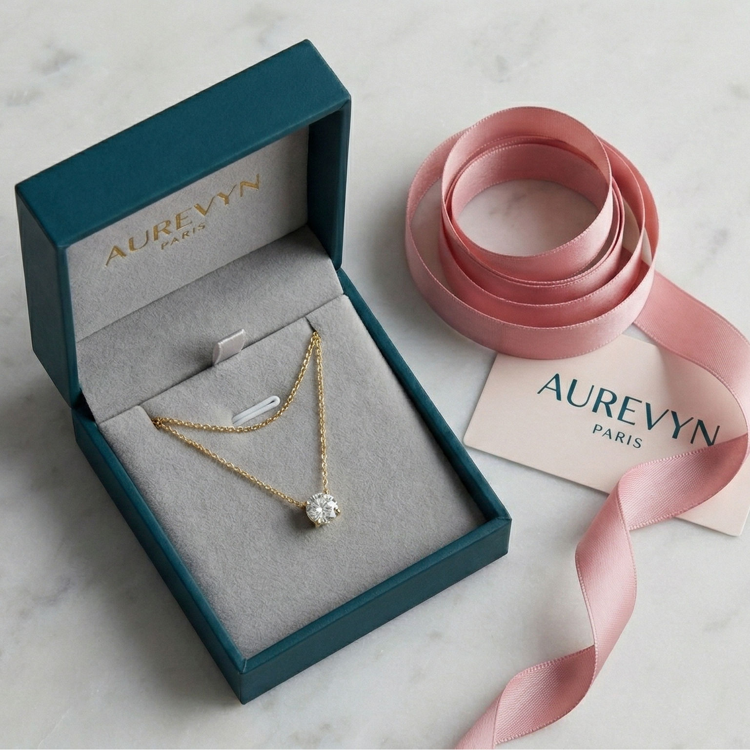 Jewelry box with a necklace and pink ribbon on a marble surface, featuring the brand 'Aurevyn'.