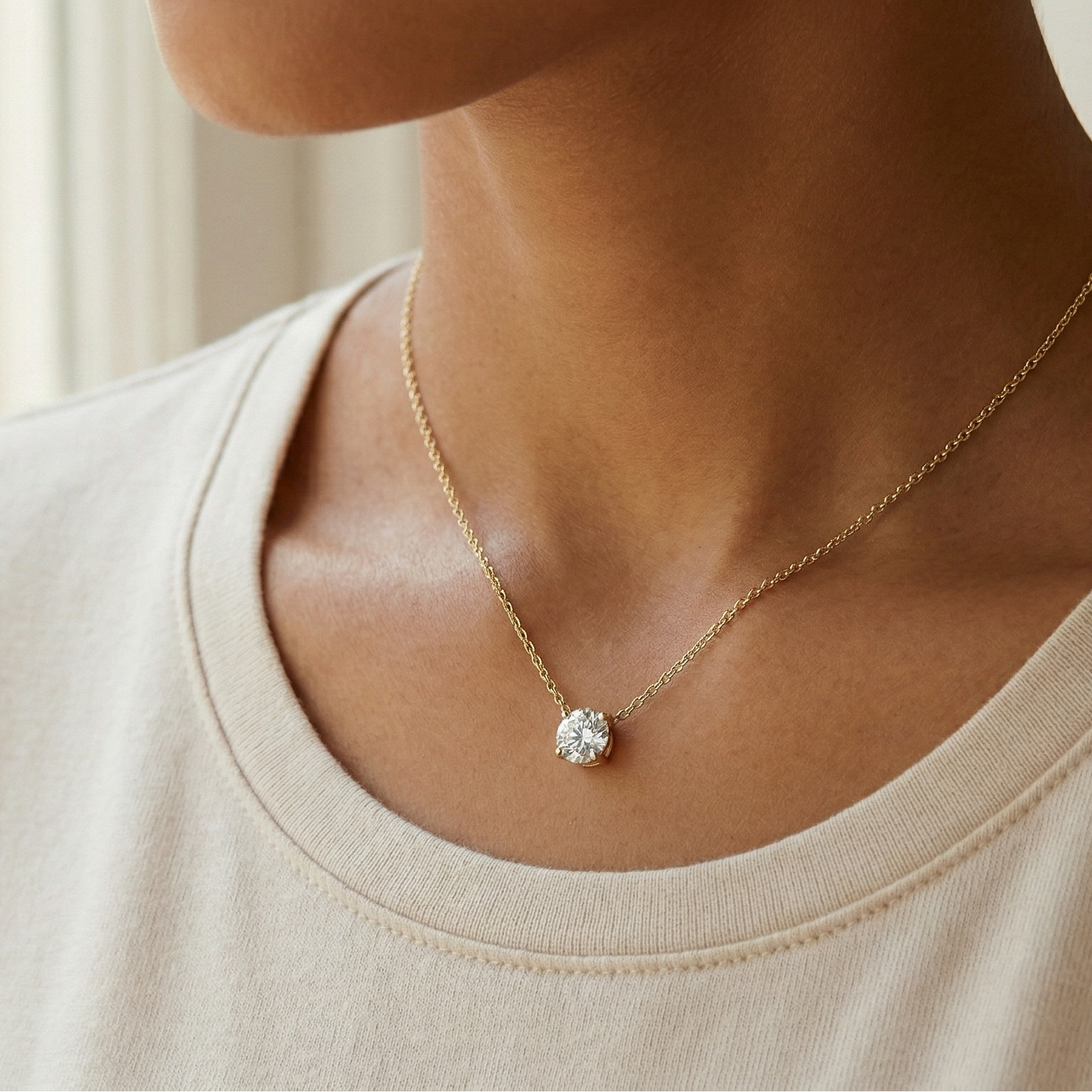 Necklace with a diamond pendant worn by a person in a beige shirt.